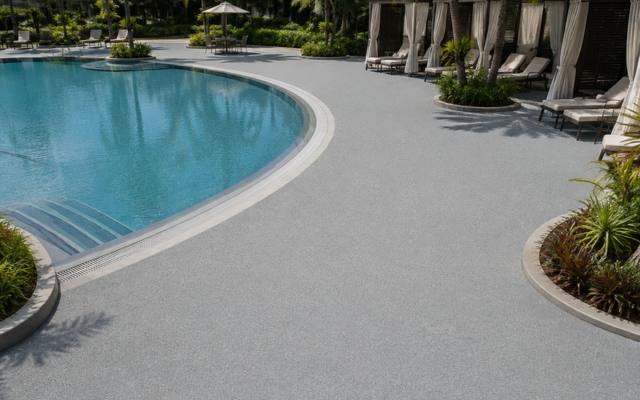 Resort pool surround finished in light grey rubber surfacing with cabanas and palms