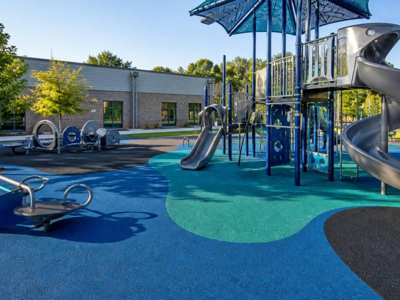 Playground slide and climber on blue rubber surfacing under a shade sail